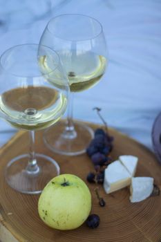 wooden stand with two glasses of champagne, grapes and camembert cheese on a white blanket in the field. picnic.