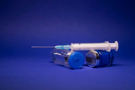 two transparent Vaccine bottle phial with no label, medical syringe injection needle. isolated on blue background. Development of coronavirus vaccine COVID-19. World race in researching. copy space