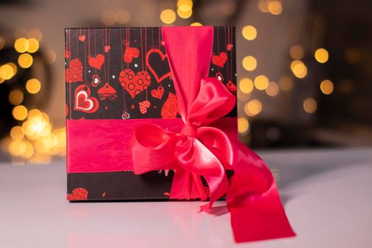 black with hearts gift box with pink ribbon bow on gold bokeh background.