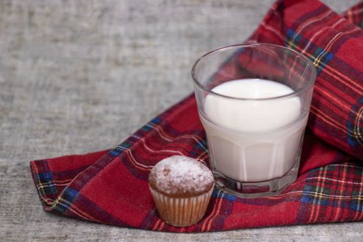cupcake or muffin in powdered sugar near a glass of milk on plaid red fabric tablecloth. healthy breakfast. snack or lunch.