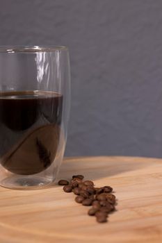 americano in a double bottom glass near coffee beans on wooden plate. coffee break.