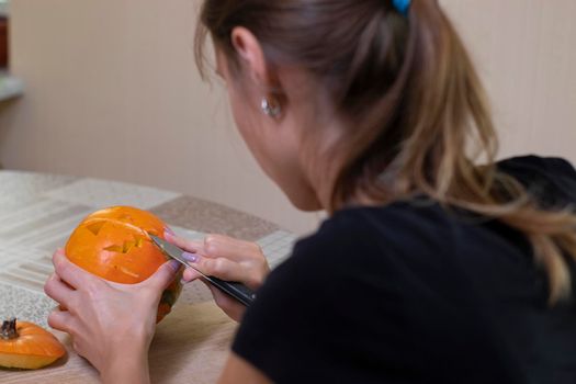 the process of making a Halloween pumpkin. cutting out the mouth by brunette girl. horror theme and Hallowe'en.