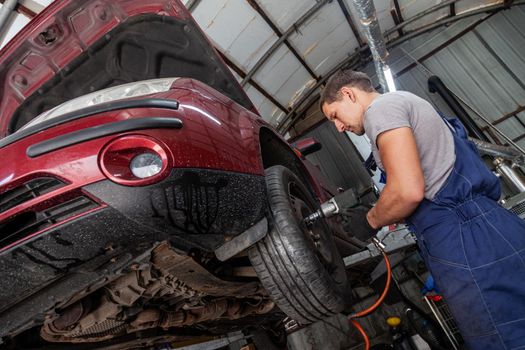 A mechanic is maintaining wheels on a vehicle in auto garage with pneumatic tool.