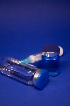 two transparent Vaccine bottle phial with no label, medical syringe injection needle. isolated on blue background. Development of coronavirus vaccine COVID-19. World race in researching. copy space