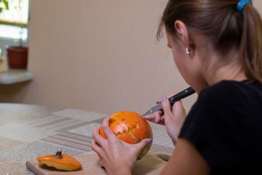 the process of making a Halloween pumpkin. cutting out the mouth by brunette girl. horror theme and Hallowe'en.