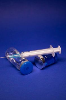 two transparent Vaccine bottle phial with no label, medical syringe injection needle. isolated on blue background. Development of coronavirus vaccine COVID-19. World race in researching. copy space