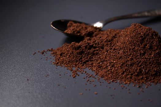 gold teaspoon in a pile of ground or instant coffee on dark background.