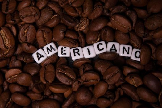 close up of Freshly roasted coffee beans near word AMERICANO written with little white cubes. top view.