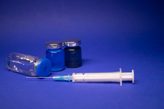 three transparent Vaccine bottle phial with no label, medical syringe injection needle. isolated on blue background. Development of coronavirus vaccine COVID-19. World race in researching. copy space