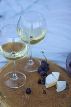 wooden stand with two glasses of champagne, grapes and camembert cheese on a white blanket in the field. picnic.