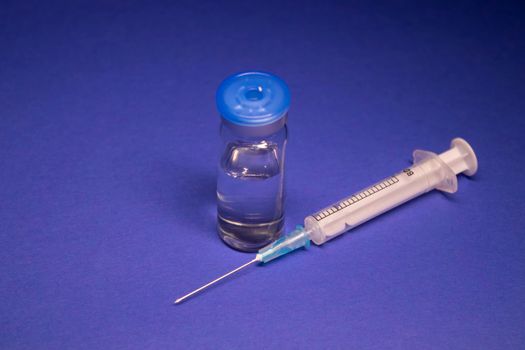 Vaccine bottle phial with no label, medical syringe injection needle. isolated on blue background. Development of coronavirus vaccine COVID-19. cure. World race in researching. copy space