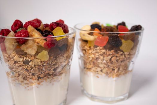 muesli dessert with yogurt and candied or dried fruits with raspberries on top in glass isolated on white background. breakfast Granola