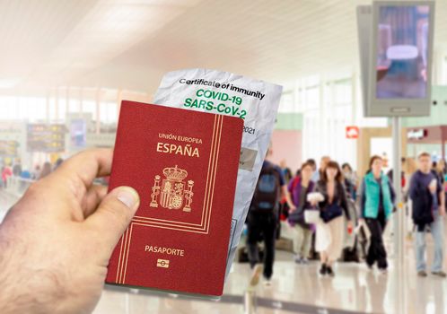 hand holding a Spain passport with a wrinkled paper Coronavirus Covid 19 immunity certificate blurred airport in the background. Immunity from Covid-19. Travel without restrictions in the EU Union