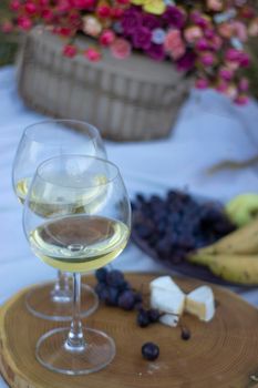 wooden stand with two glasses of champagne, grapes and camembert cheese on a white blanket in the field. picnic.