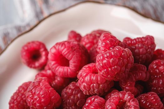 Raspberry fruits in white plate, healthy pile of summer berries, angle view macro