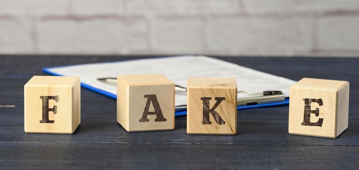 wooden cubes with the inscription fake on a blue background. The concept of information hygiene, propaganda, debunking of myths and false information. Influence of the media on public opinion