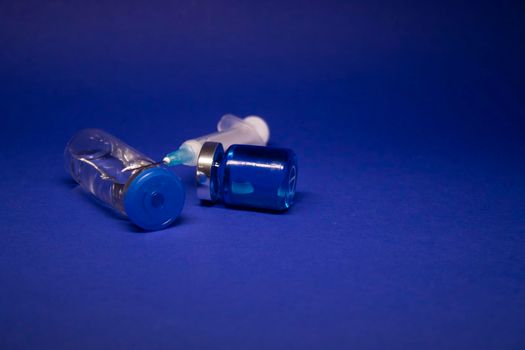 two transparent Vaccine bottle phial with no label, medical syringe injection needle. isolated on blue background. Development of coronavirus vaccine COVID-19. World race in researching. copy space