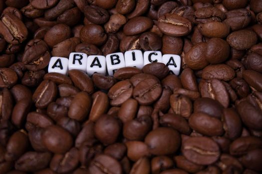 close up of Freshly roasted coffee beans near word ARABICA written with little white cubes. view from top