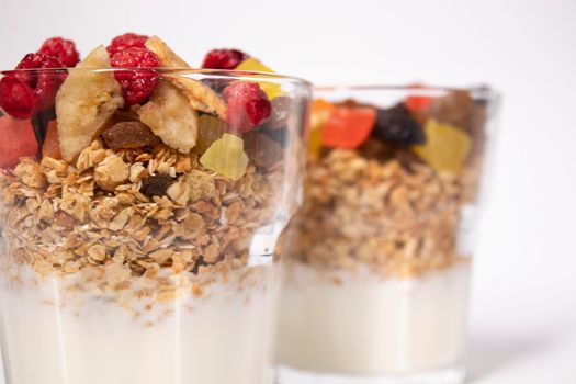 muesli dessert with yogurt and candied or dried fruits with raspberries on top in glass isolated on white background. breakfast Granola