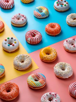 Assorted colorful glazed donuts, perspective view. Creative layout made from delicious glazed donuts. Vertical background with multicolored donuts or doughnuts. Blue, yellow and pink background