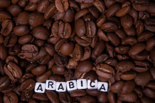 close up of Freshly roasted coffee beans near word ARABICA written with little white cubes. view from top