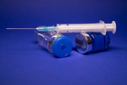 two transparent Vaccine bottle phial with no label, medical syringe injection needle. isolated on blue background. Development of coronavirus vaccine COVID-19. World race in researching. copy space