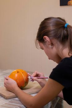 the process of making a Halloween pumpkin. drawing a layout by a brunette girl. horror theme and Hallowe'en.