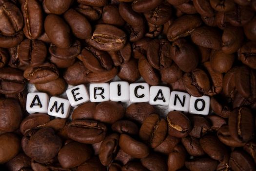 close up of Freshly roasted coffee beans near word AMERICANO written with little white cubes. top view.