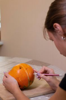 the process of making a Halloween pumpkin. drawing a layout by a brunette girl. horror theme and Hallowe'en.