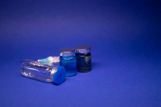 three transparent Vaccine bottle phial with no label, medical syringe injection needle. isolated on blue background. Development of coronavirus vaccine COVID-19. World race in researching. copy space