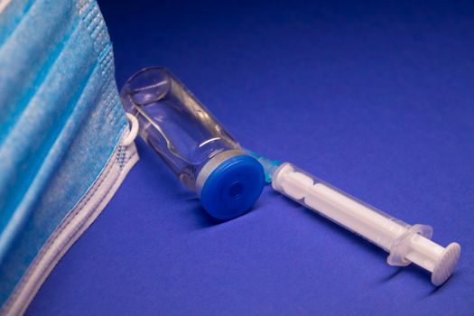 Vaccine bottle phial with no label near blue medical mask and medical syringe with injection needle. isolated on blue background. cure. Development of coronavirus vaccine COVID-19. copy space