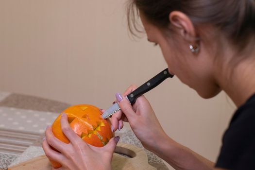 the process of making a Halloween pumpkin. cutting out the mouth by brunette girl. horror theme and Hallowe'en.