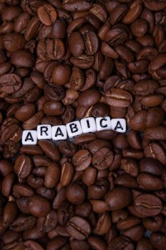 close up of Freshly roasted coffee beans near word ARABICA written with little white cubes. view from top