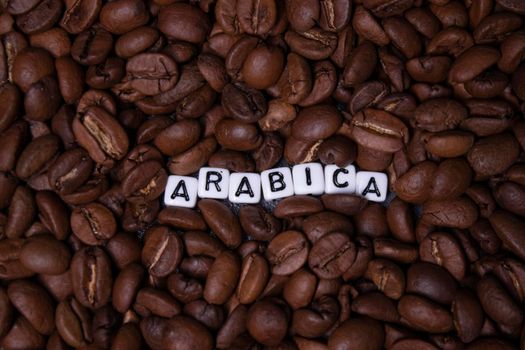 close up of Freshly roasted coffee beans near word ARABICA written with little white cubes. view from top