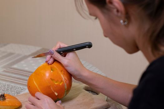 the process of making a Halloween pumpkin. cutting out the mouth by brunette girl. horror theme and Hallowe'en.