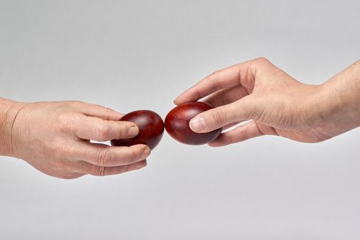 Two hands holding Easter eggs check their strength on a light background. Beat the easter eggs