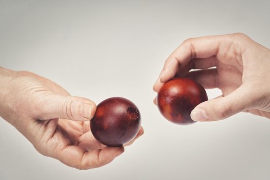 Two hands holding Easter eggs check their strength on a light background. Beat the easter eggs