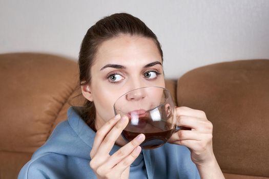 Beautiful brunette with slicked back long hair drinks coffee from a large transparent mug