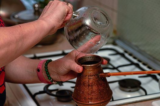 Cooking black coffee in a copper cezve on a gas stove in the kitchen at home. Close up