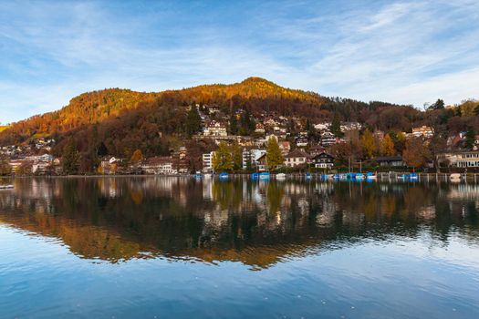 Idyllic panorama view of Thun town from Aare river side on sunny autumn day with colourful forest, Alps and blue sky cloud in background and beautiful reflection in water, Canton of Bern, Switzerland.