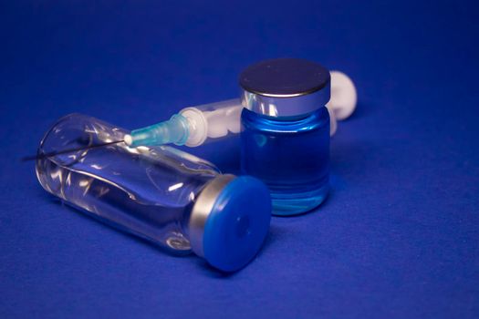 two transparent Vaccine bottle phial with no label, medical syringe injection needle. isolated on blue background. Development of coronavirus vaccine COVID-19. World race in researching. copy space