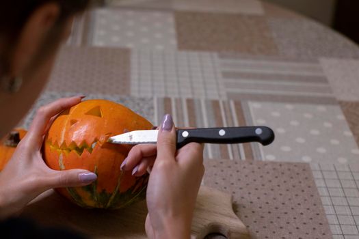 the process of making a Halloween pumpkin. cutting out the mouth by brunette girl. horror theme and Hallowe'en.