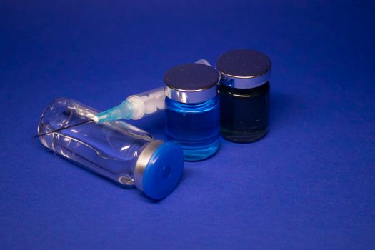 three transparent Vaccine bottle phial with no label, medical syringe injection needle. isolated on blue background. Development of coronavirus vaccine COVID-19. World race in researching. copy space