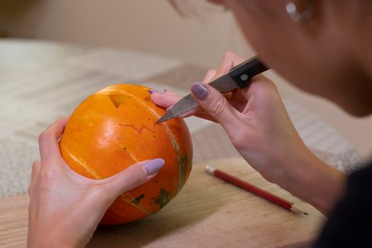 the process of making a Halloween pumpkin. cutting out the mouth by brunette girl. horror theme and Hallowe'en.