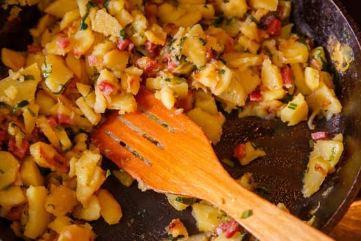 roasted domestic potatos in a frying pan with wooden spatula close-up with selective focus.