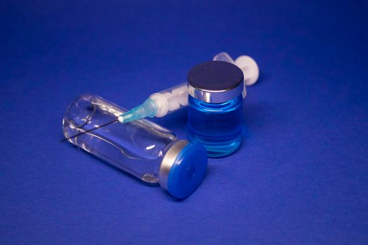 two transparent Vaccine bottle phial with no label, medical syringe injection needle. isolated on blue background. Development of coronavirus vaccine COVID-19. World race in researching. copy space