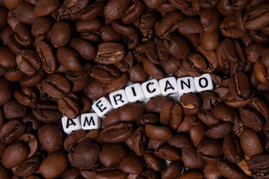 close up of Freshly roasted coffee beans near word AMERICANO written with little white cubes. top view.