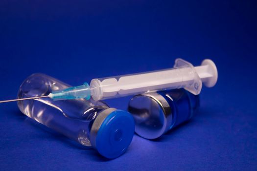 two transparent Vaccine bottle phial with no label, medical syringe injection needle. isolated on blue background. Development of coronavirus vaccine COVID-19. World race in researching. copy space