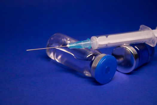 two transparent Vaccine bottle phial with no label, medical syringe injection needle. isolated on blue background. Development of coronavirus vaccine COVID-19. World race in researching. copy space