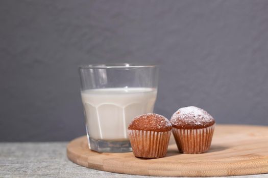 two little cupcakes or muffins in powdered sugar near a glass of milk. healthy breakfast. snack or lunch.